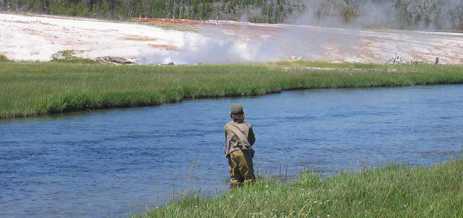 boy fishing at yellowstone with geyser in background